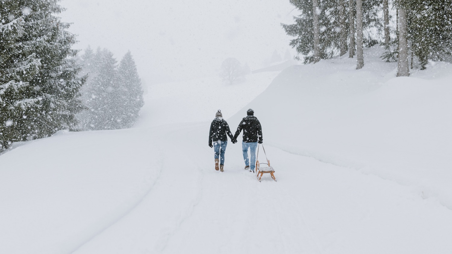 Paar spaziert mit Rodel bei Shooting im Schnee
