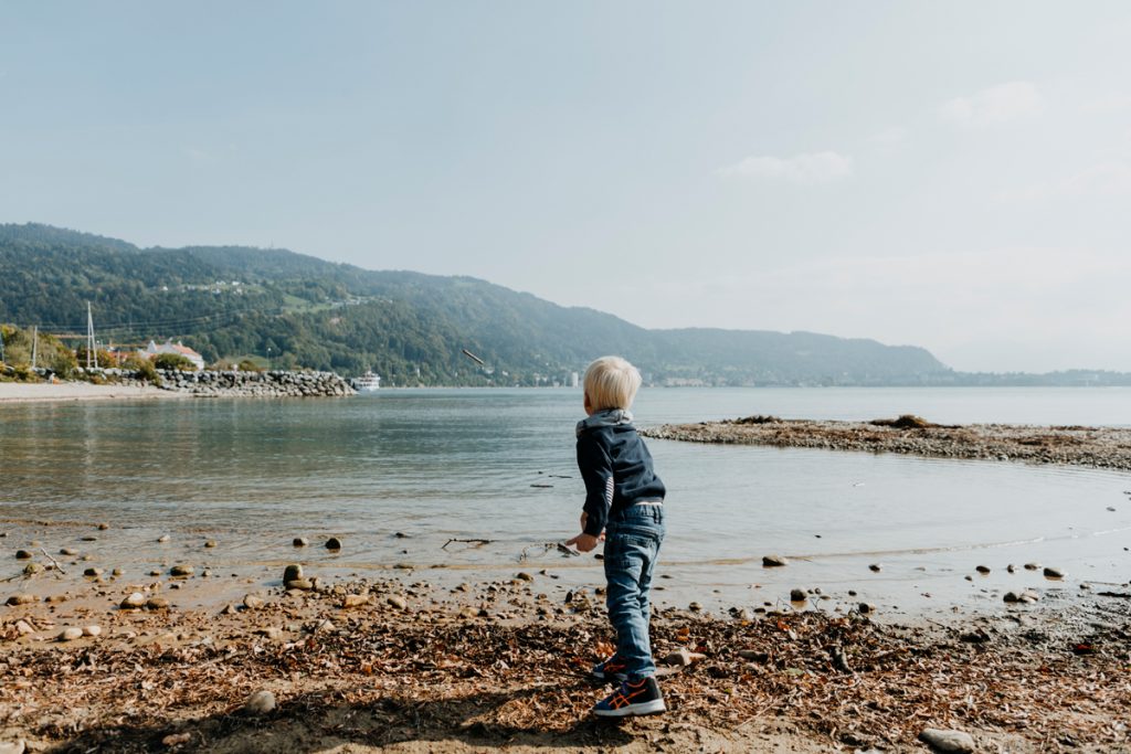 Familienfotos: Junge spielt am See mit Holz, Steinen und Wasser